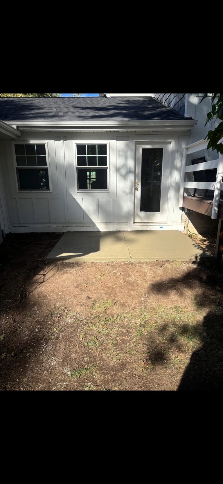 White shed with windows and door sits on concrete patio with dirt and grass yard area