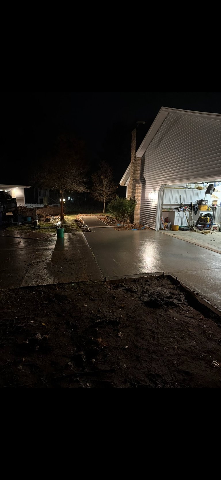 Nighttime photo of a wet driveway outside a garage with interior lighting and bare trees in background