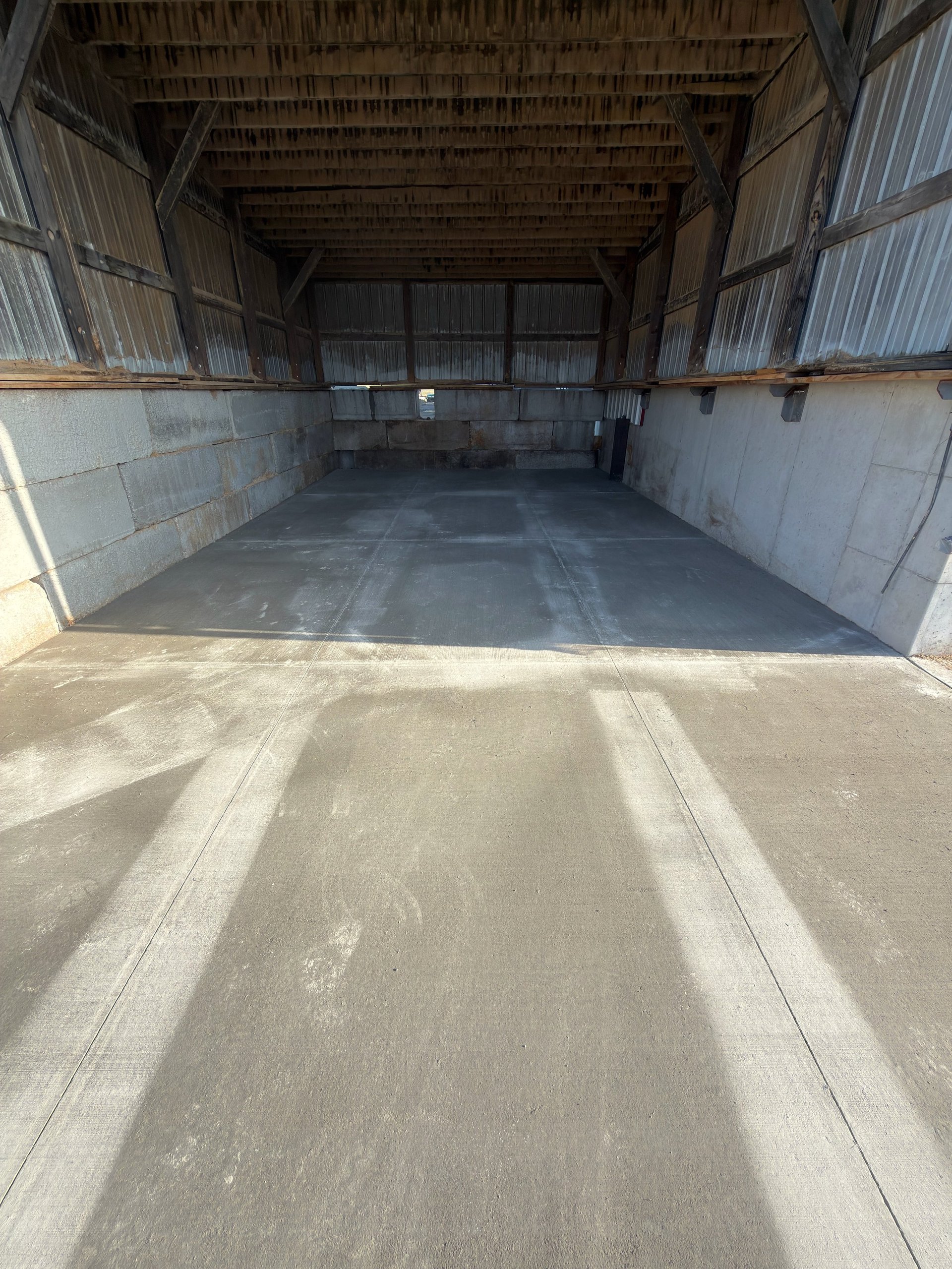 Interior view of an empty metal storage barn with open doors and concrete floor